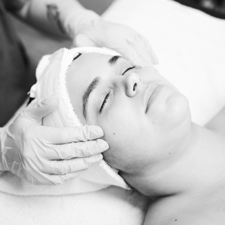 Person receiving a relaxing facial treatment with eyes closed, while a professional wearing gloves gently massages their temples.